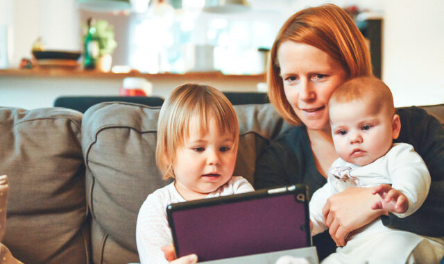 En mamma med två barn sitter i en soffa och tittar i iPad.